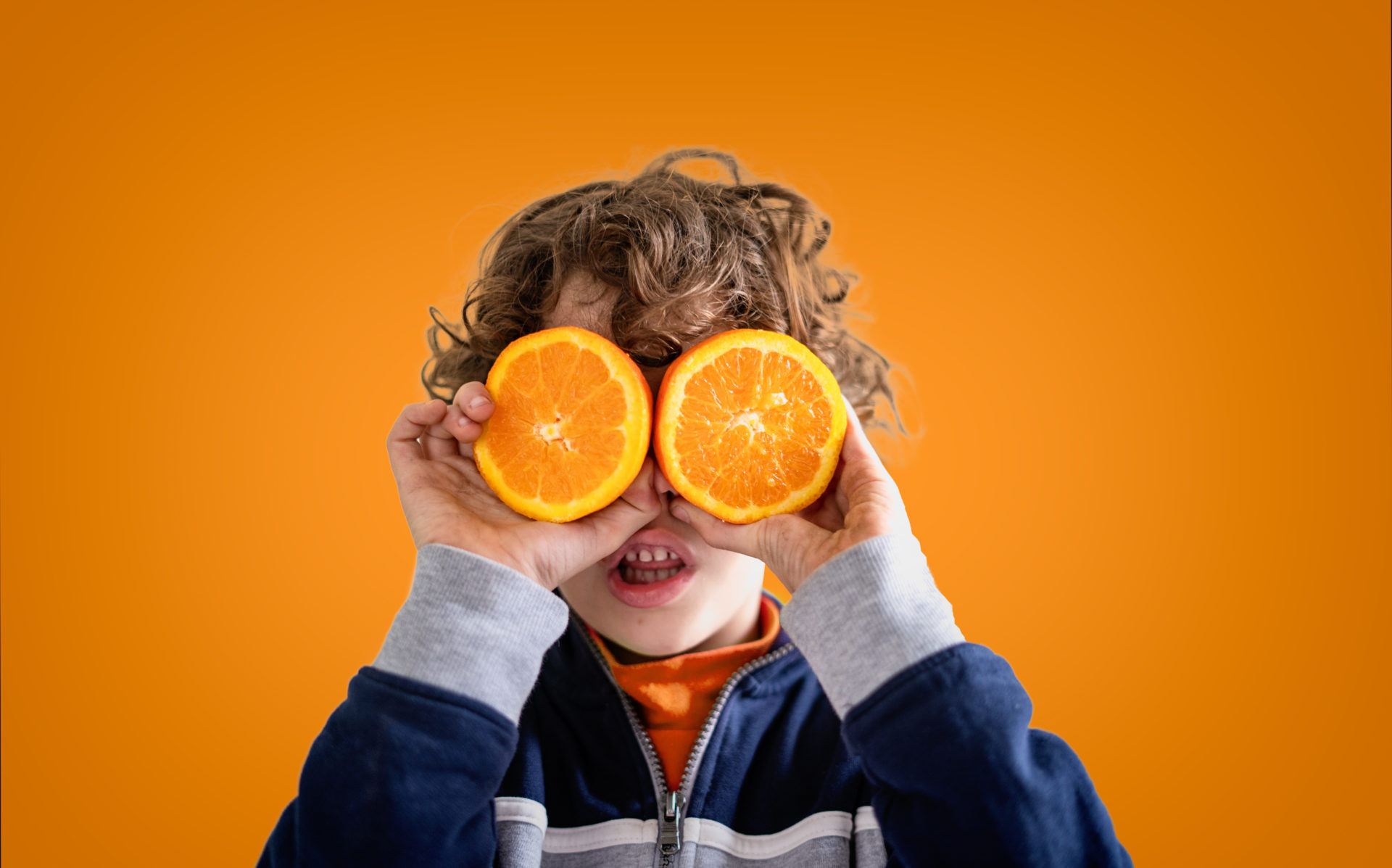 Chłopiec trzymający dwie połówki pomarańczy