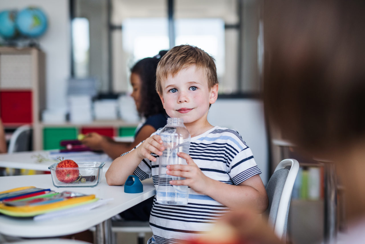 Chłopiec siedzi w szkole i pije wodę